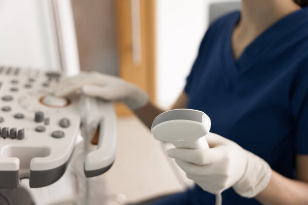 Close-up photo of ultrasonographer woman holding ultrasound transducer probe with ultrasound machine in background during diagnostic imaging procedure. Examination, prenatal care, medical technology