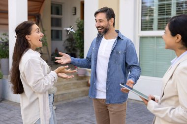 Kapalı bir anlaşma. Heyecanlı evli çift rüya evi satın almayı kutluyor kahkahalar atarak eğleniyorlar yeni evden havaya anahtarlar atıyorlar gülen emlakçıyla satış sözleşmesi imzaladıktan sonra.