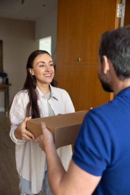 Gülümseyen bir paket geliyor. Kapıda duran kurye şirketinin sadık kadın müşterisi üniforma giymiş kibar bir teslimatçıdan karton kutuyu al.