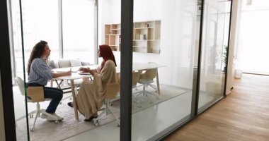 Kafkasyalı genç iş kadını Müslüman meslektaşı, iş ortağı ile konuşuyor, proje yönetimini cam duvarla toplantı odasında tartışıyor. Geniş açı, kapı aralığından gizli görüş.