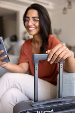 Mutlu İspanyol genç bayan turist online giriş için havayolu başvurusunu kullanıyor, otel odasında bavula dokunuyor, cep telefonuyla daktilo çekiyor, evden tatil için daire ayırtıyor. Dikey çekim