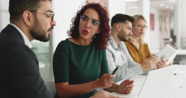 Gözlüklü ciddi bir Orta Doğulu iş kadını bilgisayardan meslektaşına iş projesini gösteriyor, ekranı işaret ediyor, konuşuyor. Bilgisayarda iş birliği yapan birkaç iş arkadaşı