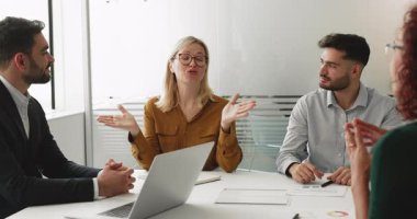 Kadın konuşmacı şirket toplantısında iş arkadaşlarıyla fikir paylaşıyor. İş kadını konferans masasında ekibe konuşuyor, yaratıcı çözüm öneriyor, iş planı üzerinde tartışılıyor.