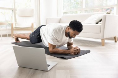 Erkekler oturma odasında minder üzerinde kalas pozisyonu alırlar, çekirdekleri, omuzları ve sırtı güçlendirmek için egzersiz yaparlar, dengeyi ve dayanıklılığı artırırlar, dizüstü bilgisayardaki beden eğitimi dersini takip ederler. Evde spor.