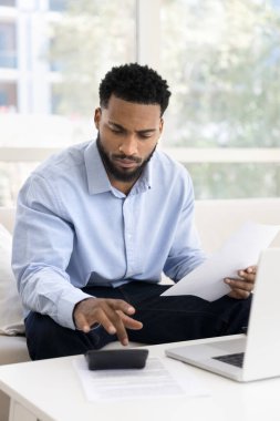 Ciddi bir Afrikalı kanepeye oturup muhasebe işlerini yapıyor. Ödenecek mali evrakları ve faturaları düzenliyor, rapor hazırlıyor, ipoteği güvenli elektronik bankacılık sistemiyle ödüyor. Dizüstü bilgisayar kullanıyor.