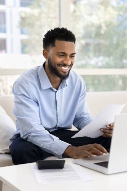 Dizüstü bilgisayarda çalışan, belgeleri tutan, kişisel mali durumları kontrol eden, mali yönetimle ilgilenen, ödeme işlemlerini yapan, işle ilgili işleri yürüten, faturaları inceleyen ya da masrafları takip eden mutlu bir adam.