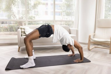 Genç Afrikalı erkekler spor kıyafetleri giyer Wheel Poose ya da Urdhva Dhanurasana oynar, evde yoga eğitimi yapar, omurgayı ve kolları güçlendirir, enerji seviyesini yükseltir, sağlıklı aktif yaşam tarzını korur.