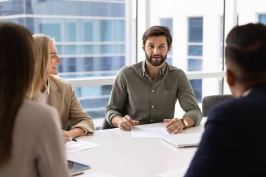İş görüşmelerinde pozitif genç işadamı, ortaklarla, iş arkadaşlarıyla, büyük masadaki yatırımcılarla konuşuyor, beyin fırtınası, ortaklık, işbirliği fikirleri sunuyor.