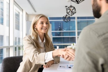 Pozitif sarışın genç iş kadını erkek iş ortağıyla anlaşma yapıyor, iş arkadaşının elini toplantı masasında sıkıyor. Kadın işveren mülakattan sonra iş başvurusunda bulunuyor