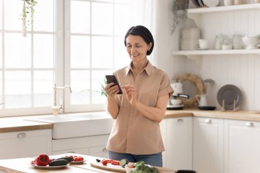 Mutfak içeriği oluşturuluyor. Gülümseyen son sınıf kadın yemek blogcusu etkileyicisi, sosyal medyada paylaşılan sağlıklı tarifler için online ana sınıfa sebze salatası hazırlama videosu çekmek için cep telefonu kullanıyor.