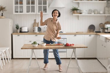 Yemek pişirme dansı partisi. Aktif enerjik son sınıf kadın ev hanımı modern mutfakta neşeyle dans ediyor disko müziğine geçiyor sağlıklı beslenme salatasını taze iştah açıcı sebzelerden hazırlıyor.