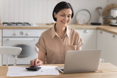 Finansal evraklar başarılı. Gülümseyen yaşlı kadın, ev mutfak işyeri inceleme kağıtlarında hesap makinesi harcamalarıyla kişisel finansman yönetiyor. Not defterinde başarılı defter tutma sonuçlarının keyfini çıkarın.