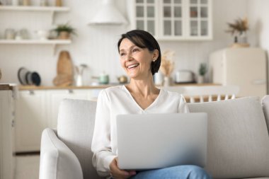 Serbest başarı hikayesi. Olumlu, mutlu, yaşlı bir kadın uzaktan kumanda defteri rahat koltukta kullan. Gururlu bir gülümsemeyle ekrandan başka yere bak. Başarılı bir iş tamamlama hayalinde güzel bir online çalışma sonucu canlandır.