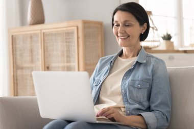 İnternette keyifli vakit geçirme zamanı. Neşeli, kendine güvenen yaşlı bayan emeklilik koltukta oturup dizüstü bilgisayarını kucağında tutarak ders saati kazanırken zevk alarak sanal internet sohbetinde dijital iletişimin tadını çıkar.