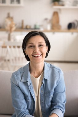 Aktif ve güzel yaşlanma. Portre mutlu, açık yürekli, modaya uygun giyinmiş, kameraya bakan, neşeli videolu sohbetler yapan evdeki koltukta canlı yayında konuşan olgun bir kadın.