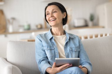Dijital eğlencenin tadını çıkarıyorum. Mutlu, güzel, yaşlı bir kadın, rahat kanepe tutacağı tablet üzerinde dinleniyor. Ekrandan uzak durun. Yaratıcı proje planlamasını, çevrimiçi öğrenim için blog hedefleri belirlemeye başlayın.