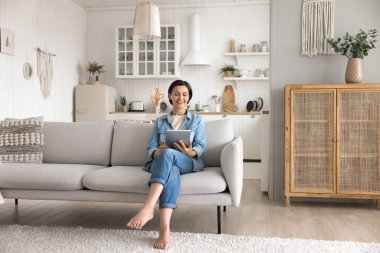 Samimi dijital emeklilik. Rahat, güzel, yaşlı bir kadın stüdyo dairesinin aydınlık sıcak oturma odasında rahat bir koltuğa oturur blogları okumak için dijital tablet kullanır parşömen haberleri, boş zamanlarında yaratıcı fikirleri araştırır.