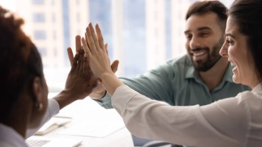 Motivasyon ve takım ruhu. Çok kültürlü üç farklı genç iş adamı iş yerinde beşlik çakarak el ele verdi. İşbirlikçi başarı eşitlik kavramını kutluyoruz