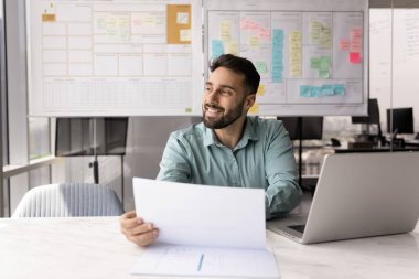 Yaratıcı planlama. Yeni başlayan genç işadamı pazarlama raporunu elinde tutuyor ofis masasında evrak işlerinden başka yere bakıyor yeni fırsatlar hayal ediyor gelecekteki proje başarısını gülümseyerek hayal ediyor. Boşluğu kopyala