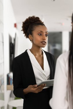 Ofis konuşması. İş yerindeki resmi kıyafet konusunda ciddi bir siyahi kadın profesyonel uzman. Genç bayanla dijital ped konuşması yap. Muayene et.