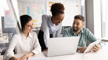 Bilgiyi kahkahalarla paylaşmak. Neşeli genç yaratıcı ekip çok kültürlü iş adamları modern planlama ofisinde birlikte çalışarak not defteri tableti arasındaki görev değişimi verilerini tartışırlar.