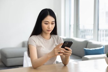 Ciddi Çinli kadın oturma odasında akıllı telefonuyla masada oturuyor, kısa videolar izliyor, haberleri izliyor, bankacılık uygulaması kullanıyor, hatırlatma yapıyor ya da iş fırsatlarını kontrol ediyor. Modern teknoloji kullanımı