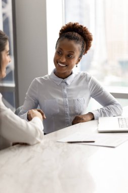 İş iletişimi başarılı. Gülümseyen genç iş kadını avukat danışmanı iş yerinde oturup müteşekkir bayan müşteriyle tokalaşıyor. Ofis toplantısında verimli bir tartışmadan sonra.