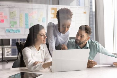 Proje geliştirme sinerjisi. Genç çok ırklı iş adamları, pazarlama çözümleri incelemek için modern ofisteki defter etrafında toplandı satış raporları Agile çalışma alanındaki araştırmaları tartıştı