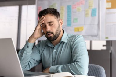 Proje baskısı altında. Stresli genç iş adamı iş yerinde kapalı gözlerle defterin önünde oturur aşırı bilgi yüklenmesinden yorgun düşer aşırı çalışmadan sonra baş ağrısı konsantrasyonu kaybına uğrar