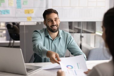 Olumlu sonuçları paylaşıyoruz. Gülümseyen genç adam finans analisti dizüstü bilgisayarın başına otur ve yazılı istatistiksel bilgileri kadın meslektaşına ver. Proje büyüme başarısını onayla.