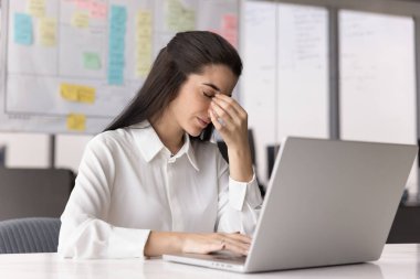 Çok fazla ekran zamanı. Yorgun ve yorgun genç bir ofis çalışanı. Masasında gözleri kapalı oturuyor. Burun köprüsünü ovuyor.