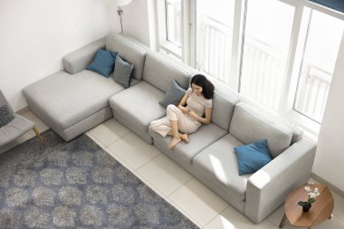 Geniş, çağdaş oturma odasında akıllı telefonlu rahat koltukta oturan genç Çinli bir kadının boş zamanlarını internette sohbet ederek ya da sosyal medyada kaydırarak geçirmesi. Modern yaşam tarzı