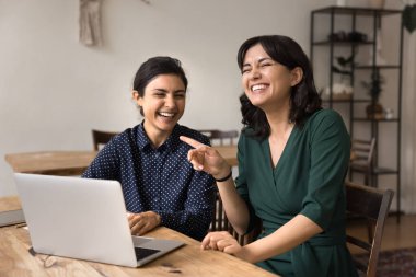 Neşeli bir takım çalışması ve dostane bir işbirliği. Çok gülen genç iş kadınları ofis masasında eğleniyorlar dizüstü bilgisayarla işe başlıyorlar eğlence şovu yaratıcı atmosferiyle iş fikirlerini tartışıyorlar