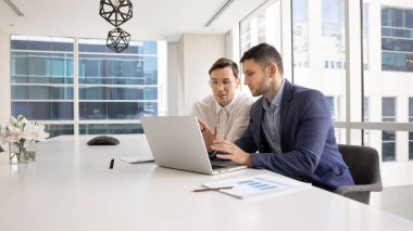 İki beyaz erkek iş arkadaşı dizüstü bilgisayar başında konuşuyor, online ürün geliştirme, internet pazarlama stratejisi, bilgisayar başında birlikte çalışıyorlar. İş adamı profesyonel meslektaşına danışıyor.