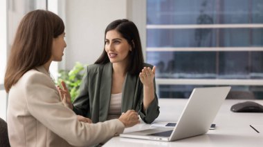 Kendinden emin genç Latin iş kadını ofis toplantı odasında iş arkadaşına danışıyor, tavsiye, profesyonel yardım, danışmanlık istiyor. İki iş arkadaşı laptopta konuşuyor.