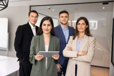 Dört başarılı iş arkadaşı bir arada duruyor, yönetim kurulunda poz veriyor, kameraya bakıyor, güven jesti yapıyor. Kadın İspanyol takım lideri elinde tablet tutuyor.