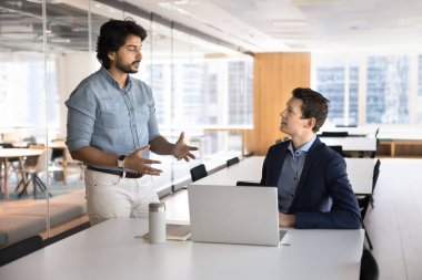 Bilgi paylaşımı. Kendine güvenen yetişkin Hintli akıl hocası takım lideri çalışma detaylarını bin yıllık çalışan stajyere açıkla. Not defterinin başında oturan erkek stajyere kariyer başarısı için rehberlik et.