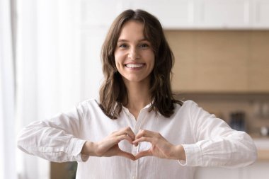 Sevgilerimle. Minnettar gülümseyen milenyum kadınının portresi. Kapalı alanda poz veriyor. Kameraya bakıyor ve parmaklarıyla yumuşak kalp hareketi yapıyor. Gönüllü hayır kurumu minnettarlık nezaket destek konsepti