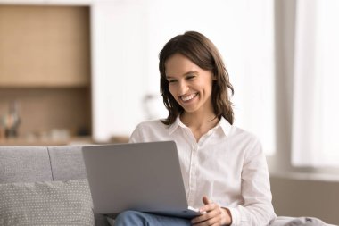 İş ve eğlence için dizüstü bilgisayar. Gülümseyen genç kız rahat kanepeye otur ve video üzerinden sohbet etmek için not defteri kullan. Dijital sohbetin tadını çıkar. Yaratıcı serbest proje üzerine çalış.