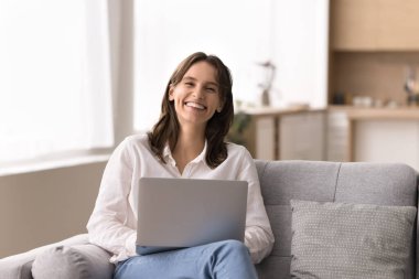 Üretken uzaktan kumanda ya da öğrenme. Gülümseyen, gururlu genç bir kadın, rahat evinde koltukta oturmuş elinde bir not defteri tutarak başarılı bir serbest çalışma projesiyle tatmin oluyor.