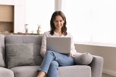 Sıradan bir dijital eğlence. Oturma odasındaki rahat kanepede gülümseyen genç bir bayan dinlenme odası. Not defterindeki web siteleri. Ders programları. İnternet makaleleri.