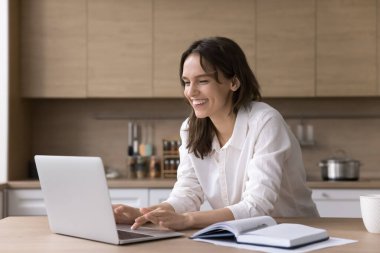 Uzaktan çalışma ya da öğrenim. Güzel, gülümseyen, serbest çalışan genç bir bayan öğrenci ev ofisinden öğrenim görüyor online arama bilgileri web siteleri Not Defteri kullanarak e-posta inceleme verilerini kontrol ediyor