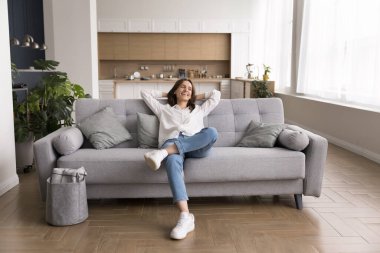 Güzel bir ev eğlencesi. Tam uzunlukta gülümseyen, tasasız genç bir kadın temiz, rahat, modern bir dairede koltukta dinleniyor. Yeni bir dekorasyon yaptıktan sonra iç dekorasyonun keyfini çıkarıyor.