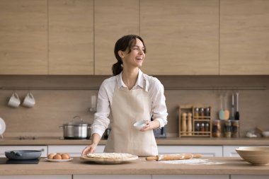 Kendine güvenen bir aşçı. Önlüklü mutlu genç kadın ev yapımı pizza pastası hazırla kahkahalarla hamurdan uzaklaş çağdaş ev mutfağında öğle yemeği pişirmenin tadını çıkar.