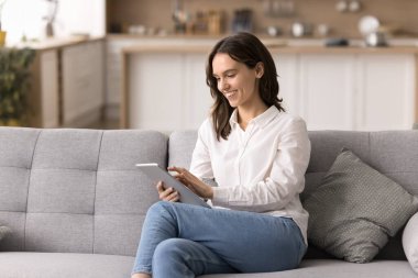 Evde günlük tablet kullanımı. Kendine güveni tam genç bir kadın evdeki rahat koltukta bilgisayarını kullanmaktan zevk alıyor. Uzaktan bağımsız çalışıyor, e-kitap okuyor, dijital içerik videoları seyrediyor.