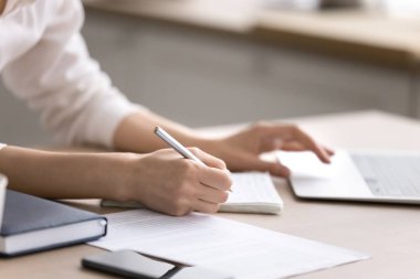 Çalış ve araştır. Kapalı kadın elleri kalem tutarken defter ekranı basılı kağıt dökümanlarını kontrol ediyor. Sınav kavramına hazırlanan harmanlanmış uzaktan eğitim bilgi araması