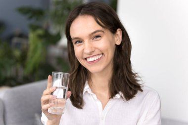Sağlıklı hidrasyon alışkanlığı. Portre mutlu genç bir kadın kameraya bakıyor. Elinde saf içme suyu bardağı var. Kişisel bakım reklamı yapıyor günlük yaşam enerjisini filtreliyor.