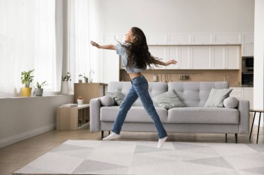 Hava yürüyüşü macerası. Geniş modern oturma odasında fantezi oyunlarından hoşlanan uzun boylu, aktif bir genç kız kollarını açmış, bacaklarını açmış, havada uçuyormuş gibi yapıp saf mutluluğun tadını çıkarıyor.