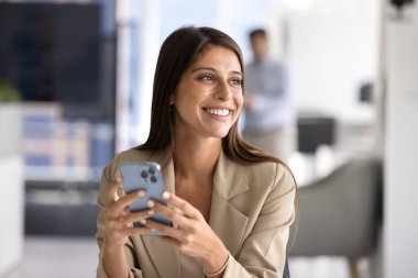 Mutlu, güzel İspanyol menajer kadın cep telefonu tutuyor, iş yerindeki cep telefonuyla yazı yazıyor dişlek gülümsemesiyle yüzünü çevirimiçi iletişim için teknolojiyi kullanıyor.