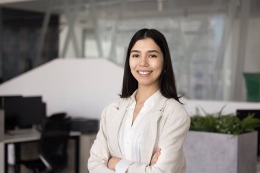 Mutlu, kendinden emin, genç Orta Doğulu iş kadını kollarını kavuşturmuş, dişlek gülümsemesiyle kameraya bakıyor. Pozitif Asyalı iş kadını, kadın profesyonel vesikalık.